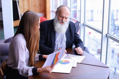 Yaşlı patron adam işaretleri belge raporları ile genç asistanı ile