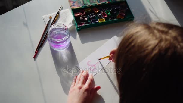 Malerin schreibt mit Pinsel und Farbe Inschrift auf Blatt, sitzt tagsüber am Tisch mit Kunstmaterialien in der Werkstatt.
