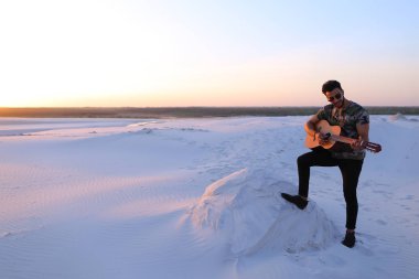 Arap yakışıklı arasında kum tepe üzerinde duran gitar çalmak