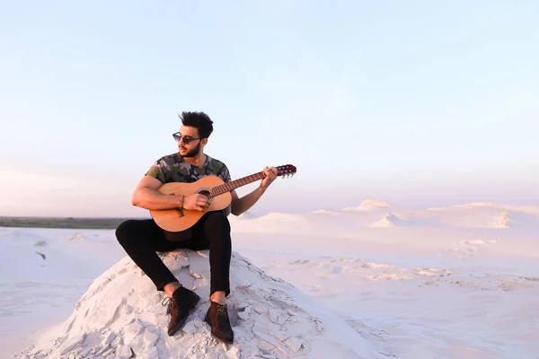 Attraktive arabische Kerl singt Lieder auf der Gitarre, sitzt auf Hügel in — Stockfoto