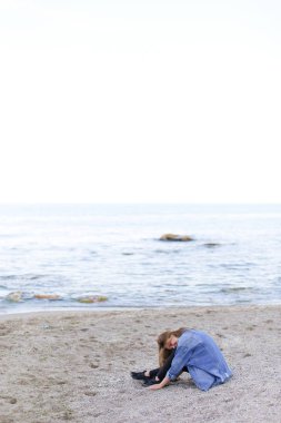 Gülümseyen genç kadın kumsalda aittir ve kamera, oturan pozlar