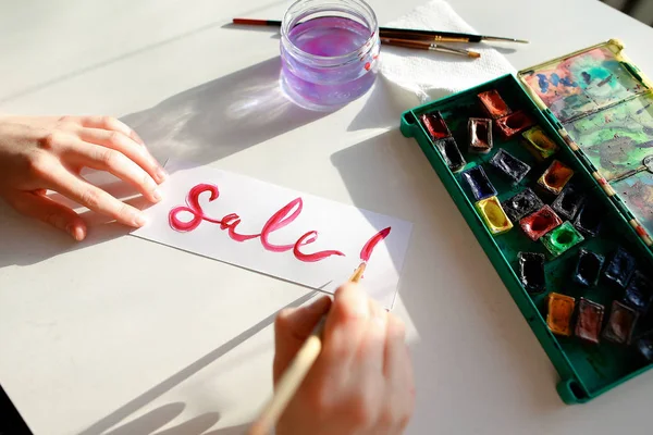Κορίτσι ζωγράφος γράφει με βούρτσα και χρωματίζει επιγραφή σε φύλλο, — Φωτογραφία Αρχείου