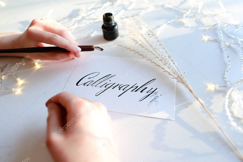 Female master of lettering of ink writes word on paper, sitting