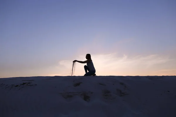 Beautiful girl sits at crouching on sandy desert hill on sunset