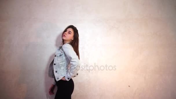 Mulher bonita com sorriso posando na câmera, de pé no fundo da parede de luz . — Vídeo de Stock