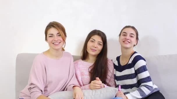 三个有吸引力的年轻朋友和相机的笑容，坐在沙发上在明亮的卧室里的合影. — 图库视频影像