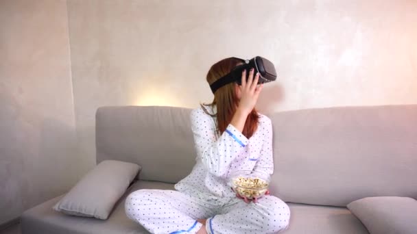 Menina legal assiste vídeo em óculos VR, sentado no sofá no quarto brilhante à noite . — Vídeo de Stock