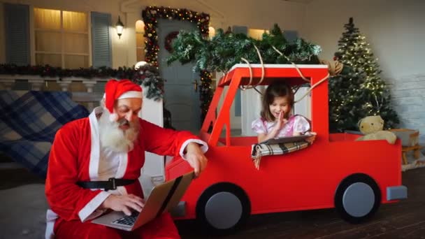 Веселый Санта-Клаус с ноутбуком и маленькой девочкой, играющей на планшете . — стоковое видео
