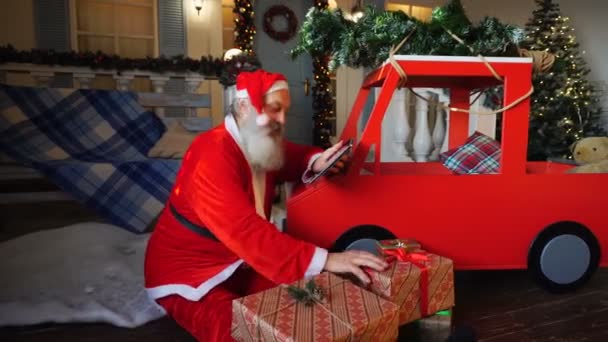 圣诞老人查看平板电脑上的礼物清单, 并把礼物放进车里. — 图库视频影像