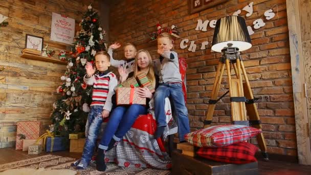 The three brothers and sister sit on armchair near Christmas tree and smile — Stock Video