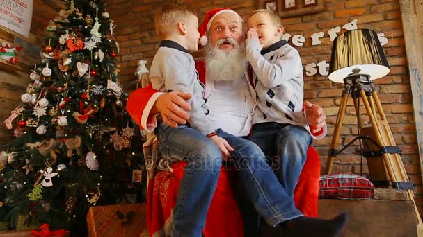 En Santas rodillas se sientan hermanos gemelos y cuentan divertida historia — Vídeos de Stock