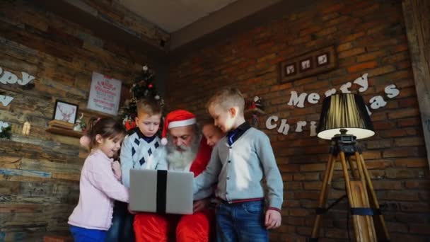 Enge Freunde von Kindern mit Weihnachtsmann benutzen Laptop im weihnachtlich geschmückten Zimmer mit hohem Weihnachtsbaum — Stockvideo