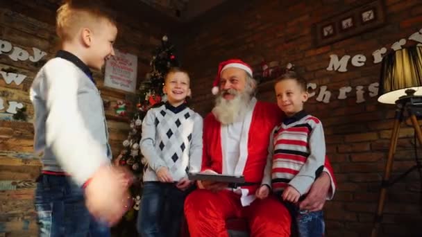 Little brothers boys teach Santa Claus to play on tablet in festively decorated room with decorated Christmas tree — Stock Video