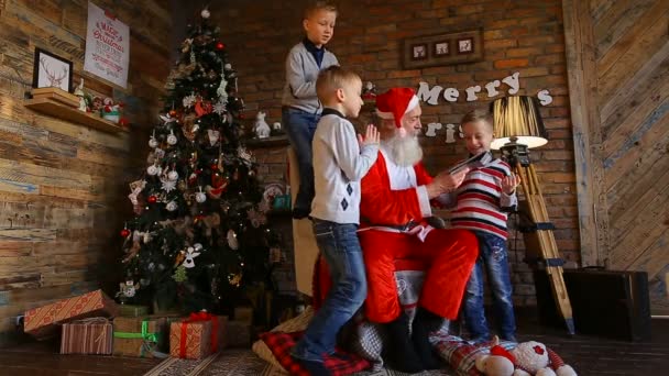 Tres amigos muestran dibujos animados de Santa Claus en la tableta en la habitación decorada para Navidad con un árbol exuberante — Vídeos de Stock