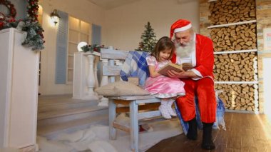 Keskin küçük kız Noel dedesi ile büyük kitap tutan ve Bahçe süslemeleri ile yakındaki bankta oturur