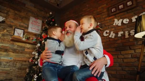Boldog fiúk testvérek egyidejűleg suttogás a fül, a Mikulás karácsony kívánja szépen díszített szoba — Stock videók