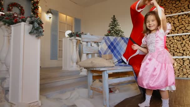 Lyckligt kvinnliga barn dansar bredvid jultomten, som sitter på bänken nära stora gården — Stockvideo