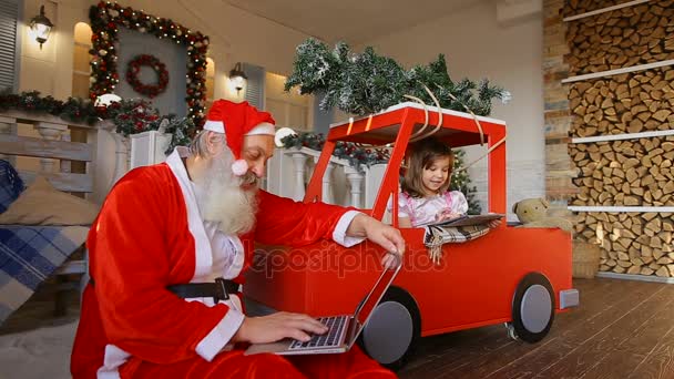 Père Noël et mignonne petite fille choisir des cadeaux, assis sur le porche décoré pour Noël à la maison — Video