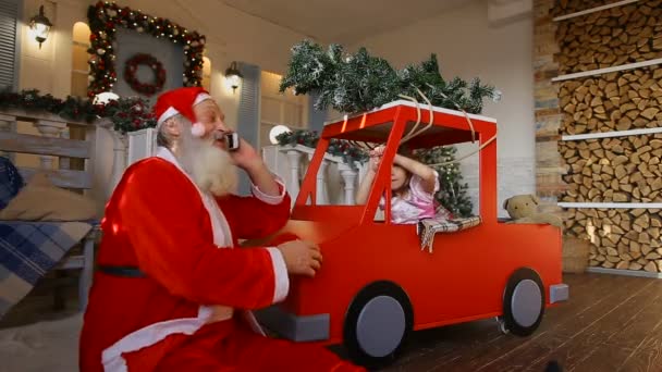 O avô de Natal e a pequena criança enviam congratulações pelo telefone, sentado no alpendre da casa decorada — Vídeo de Stock