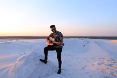 Arap yakışıklı arasında kum tepe üzerinde duran gitar çalmak