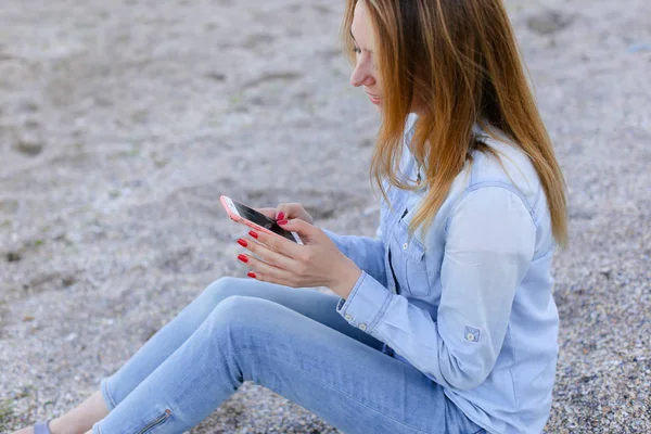 Hermosa chica charla por teléfono con sonrisa y se sienta en la playa n — Foto de Stock