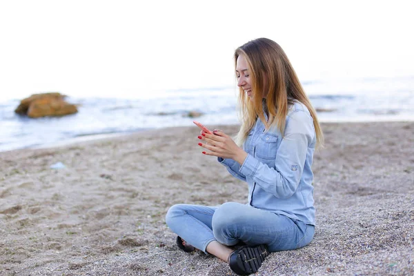 Hermosa chica charla por teléfono con sonrisa y se sienta en la playa n — Foto de Stock