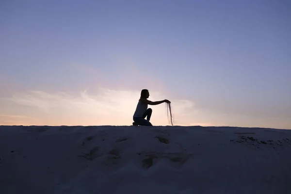 Belle fille est assise à s'accroupir sur une colline sablonneuse du désert au coucher du soleil — Photo