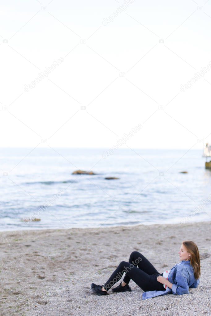 Smiling young woman rests on beach and poses in camera, sitting