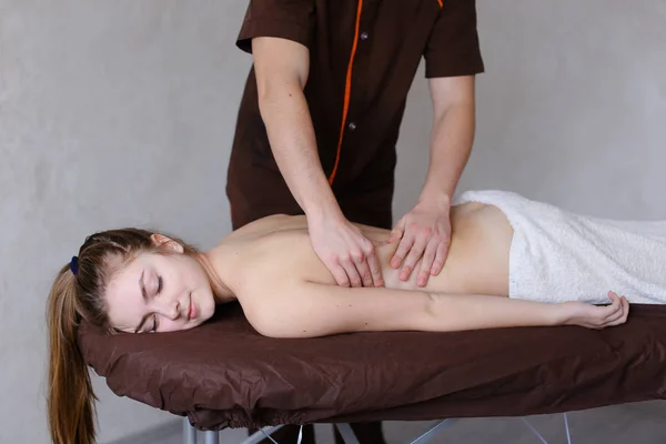 Leuke vent masseur kneedt achterkant vrouwelijke patiënt die op Bank ligt — Stockfoto