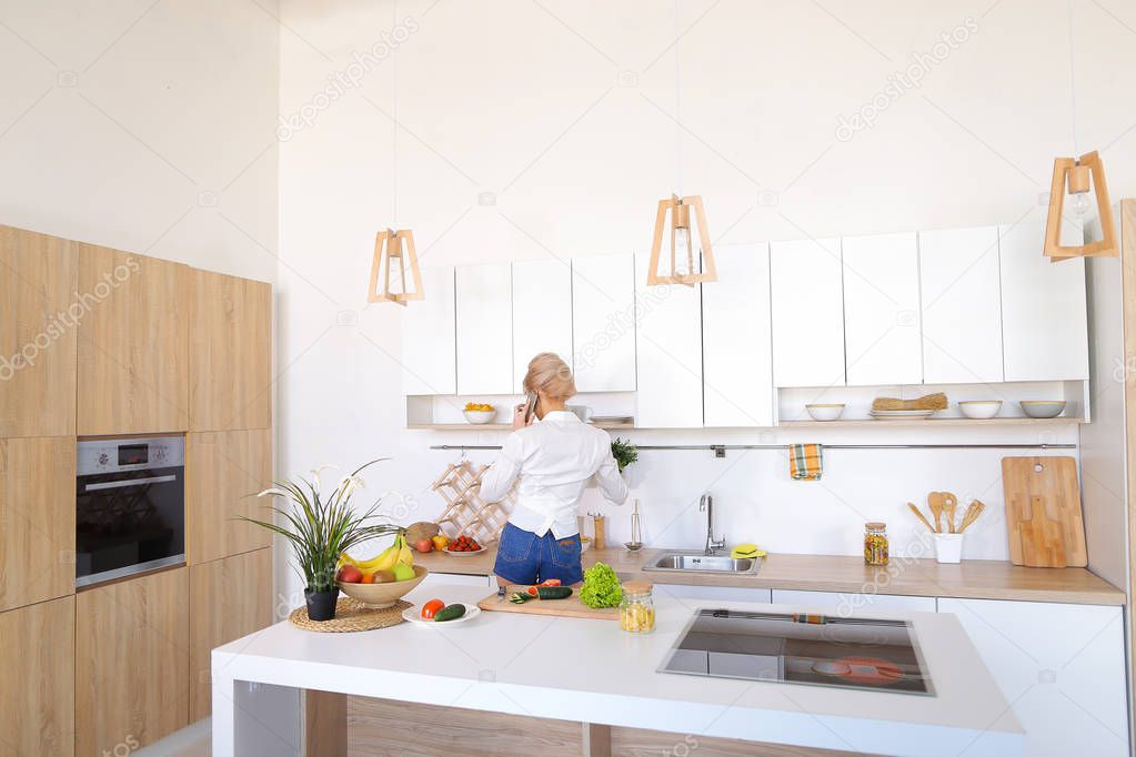 Charming girl talking on phone and preparing dinner in stylish k