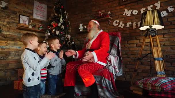 Три маленьких мальчика рассказывают Санта-Клаусу смешные истории в украшенной праздничной комнате — стоковое видео