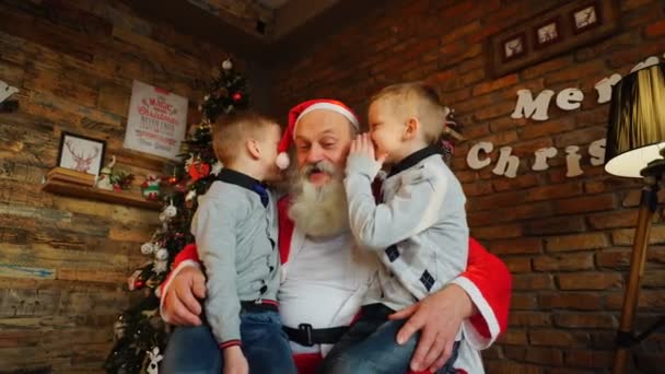 Two twin boys alternately make wish in ear of Santa Claus in decorated room for Christmas — Stock Video