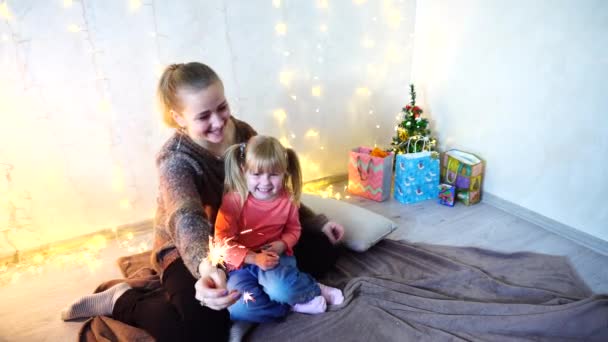 Communication of older female sister with youngest girl who spend time together and sitting on floor in room on background of wall with garland and small tree. — Stock Video