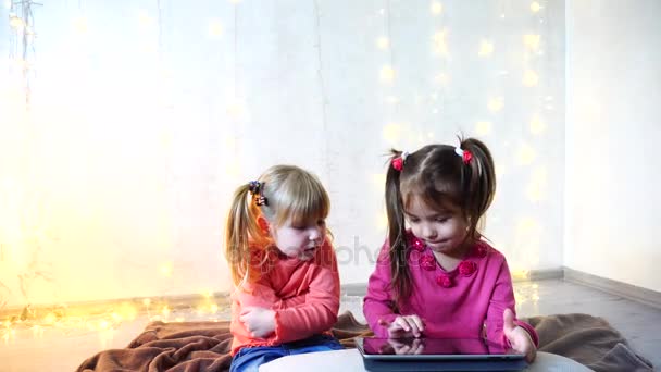 Malé holčičky, které se podílejí na využívání tabletu a sedět na podlaze ve světlé místnosti s věnec na zeď. — Stock video