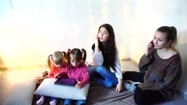 Oudere vrouwen en baby meisjes vier communiceren en bezig met eigen zaken, zittend op de vloer op de achtergrond van de muur met garland op kamer. — Stockvideo