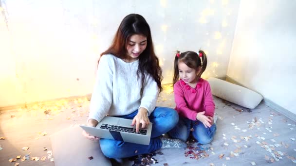 Comunicazione della sorella maggiore con la ragazza più giovane seduta al piano in camera sullo sfondo del muro con ghirlanda e piccolo abete . — Video Stock