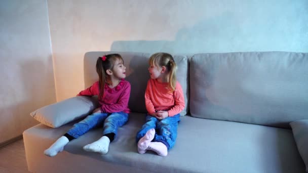Två små flickor sitter på soffan och spelar, visar varandra tungor — Stockvideo