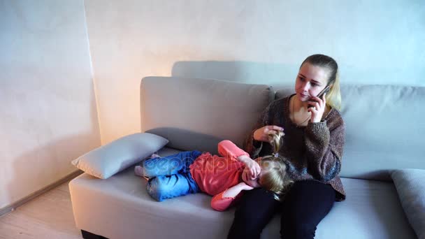 Mladá matka sedí na gauči v obývacím pokoji, malou dceru leží na kolenou žena