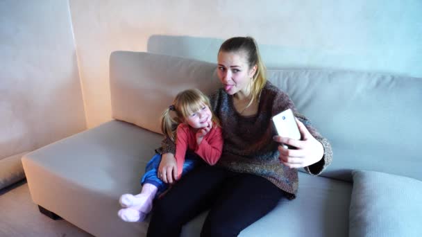 Giovane madre di discendenza americana si siede sul divano con figlia piccola e fa foto sul telefono . — Video Stock