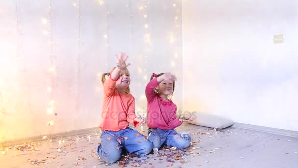 Két kis lány pózol a kamera, gyermekek integetett a kezével, és dobja fel konfetti. — Stock videók