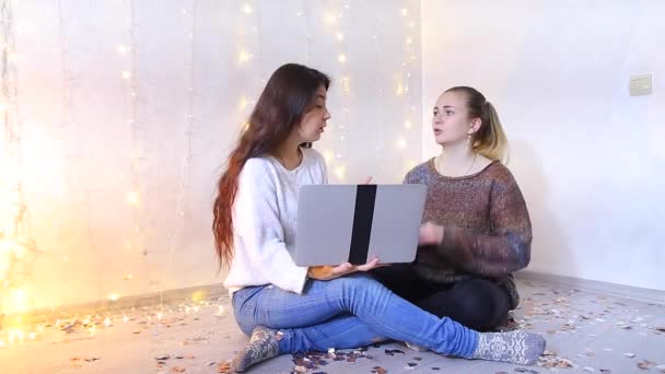 Две красивые молодые женщины сидят на полу в гостиной и выбирают подарки родственникам к праздникам через ноутбук . — стоковое видео
