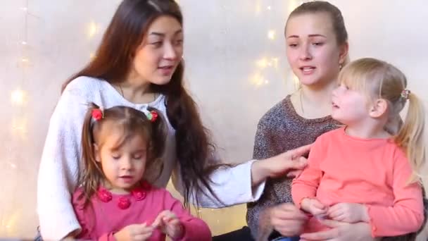 Two moms with small daughters sit on floor and talk with relatives through video communication. — Stock Video