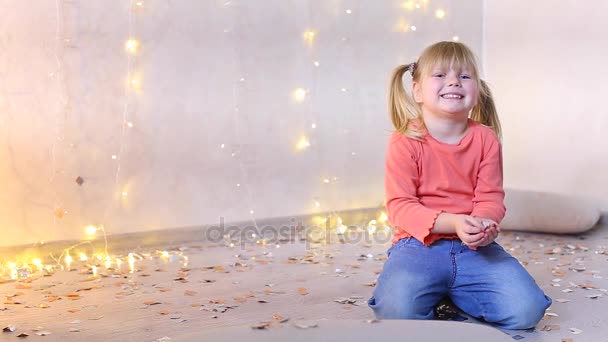 Kleines Mädchen von europäischem Aussehen sitzt auf dem Boden im Fotostudio mit Silvesterdekor. — Stockvideo