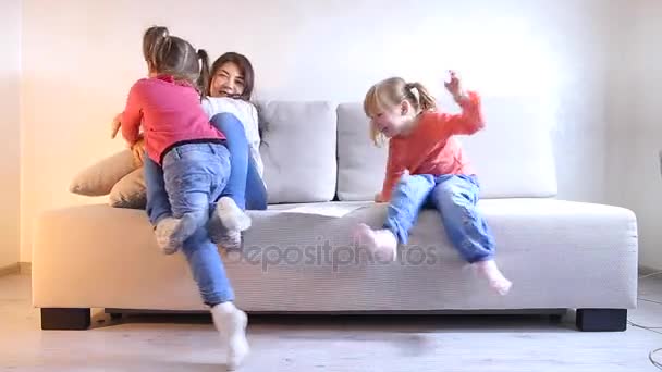 Young beautiful mom sitting on couch and playing with two daughters — Stock Video