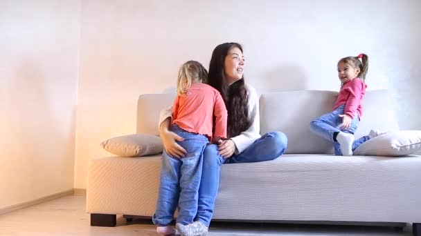 Młoda matka z dwoma córkami odgrywa na kanapie w salonie. — Wideo stockowe