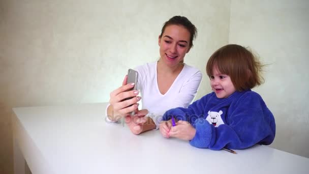 Jovem mãe e filha brincando com a câmera do telefone, meninas sentadas e usando efeitos engraçados da câmera . — Vídeo de Stock