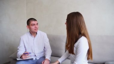 Genç kadın kim dinler ve yazıyor doktor görmeye geldim. Adam ve tıbbi ofis gri duvar arka plan üzerinde kanepede oturan kadın.