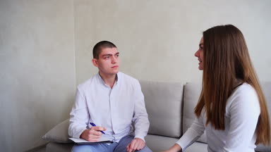 Genç kadın kim dinler ve yazıyor doktor görmeye geldim. Adam ve tıbbi ofis gri duvar arka plan üzerinde kanepede oturan kadın.