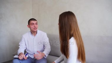 Genç kadın kim dinler ve yazıyor doktor görmeye geldim. Adam ve tıbbi ofis gri duvar arka plan üzerinde kanepede oturan kadın.