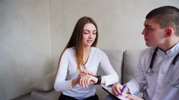 Guy nefrologista e paciente feminino estudam funções médicas do relógio inteligente, usam novas tecnologias no escritório do hospital . — Vídeo de Stock